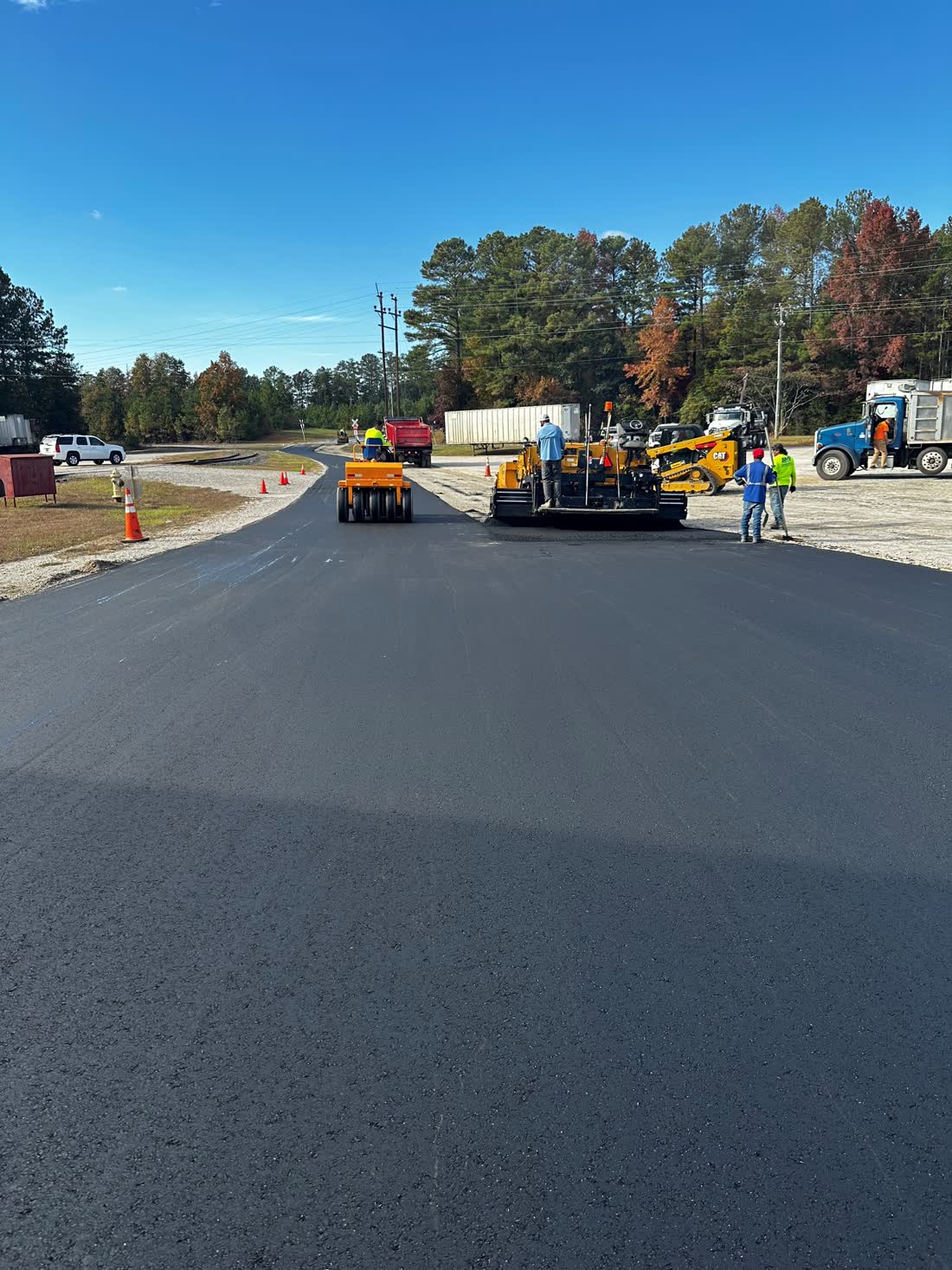 Paver machine laying a fresh lift of hot mix asphalt with trees in the background