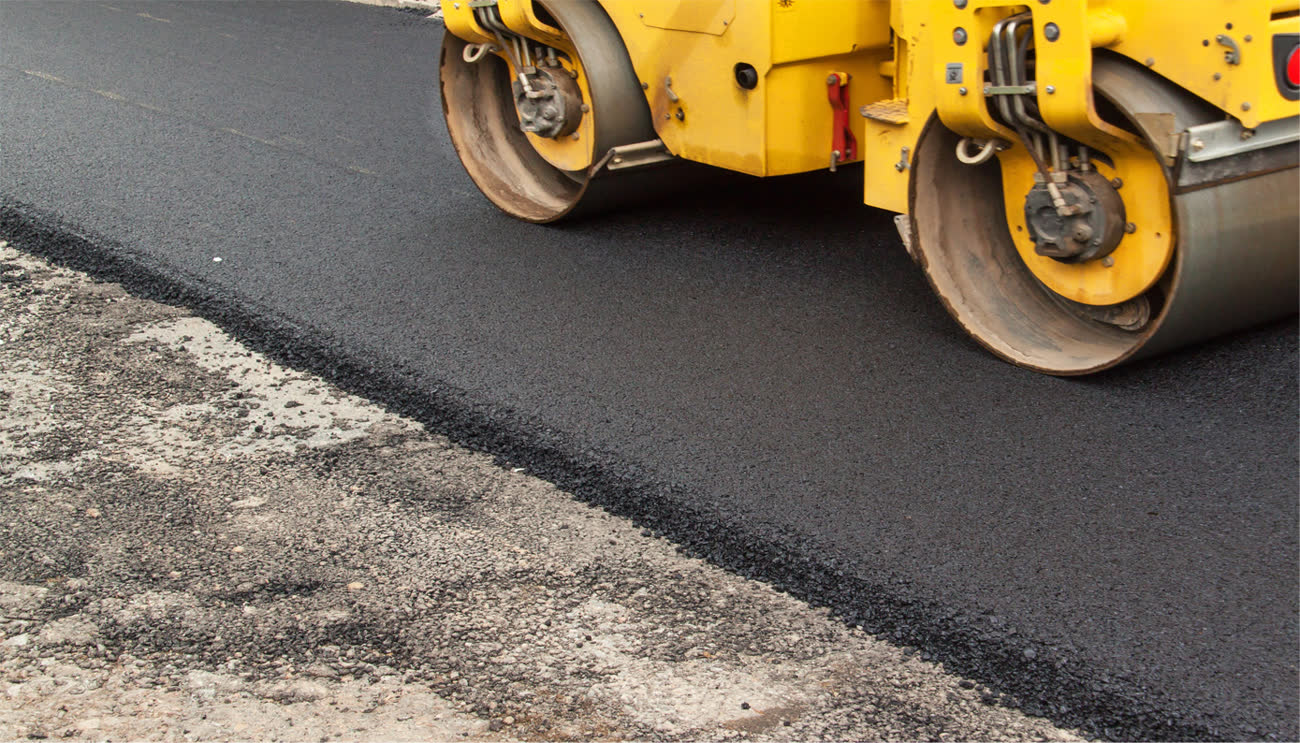Close-up of a yellow compactor rolling a fresh edge of hot mix asphalt
