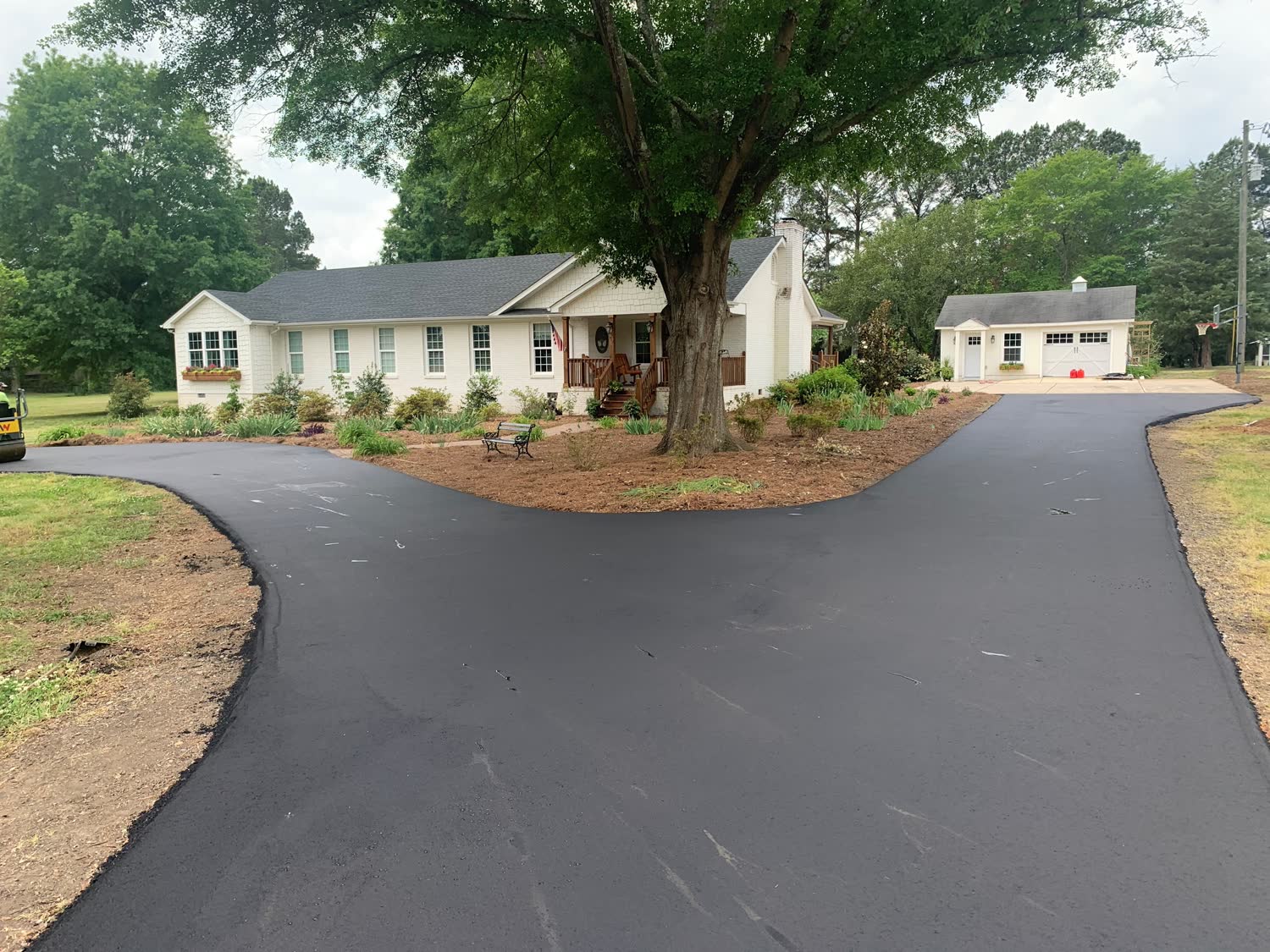 Freshly paved asphalt driveway curving around a Pacific Northwest home framed by evergreens